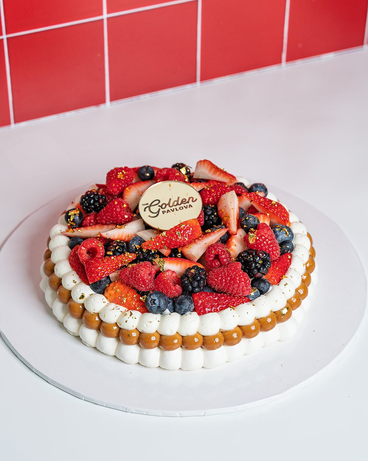 Overhead view of mixed berries pavlova by The Golden Pavlova, topped with strawberries, blueberries, raspberries, whipped cream and golden flakes, handmade in Miami.